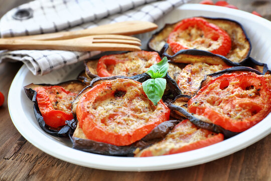 Delicious vegetarian pizza topping, roasted aubergine with tomatoes and basil on the plate on the wooden table, healthy and tasty eating