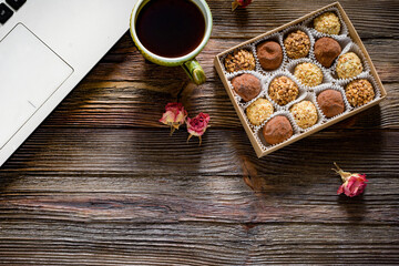 Design mock up: laptop, box of chocolate candies and cup of black coffee on wooden table. Copy...