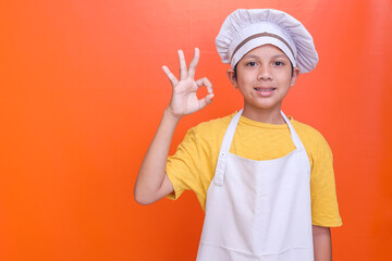 Adorable little boy chef showing ok-sign perfect delicious taste gesture isolated over orange color background with copy space for text