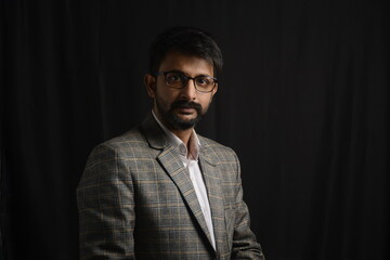 Fototapeta premium Portrait of happy corporate dressed up person in suit and wearing specs portraying different moods. Low key shoot of bearded office man well suited. Black background.