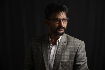 Portrait of happy corporate dressed up person in suit and wearing specs portraying different moods. Low key shoot of bearded office man well suited. Black background.