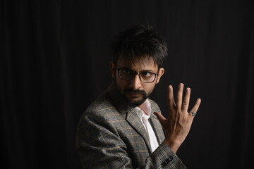 Portrait of happy corporate dressed up person in suit and wearing specs portraying different moods. Low key shoot of bearded office man well suited. Black background.