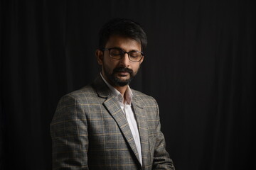 Fototapeta premium Portrait of happy corporate dressed up person in suit and wearing specs portraying different moods. Low key shoot of bearded office man well suited. Black background.