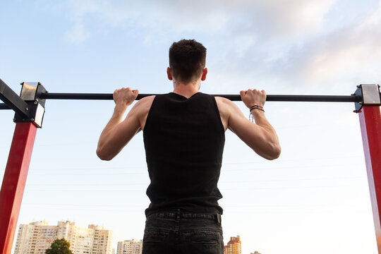 Athlete doing pull-up on horizontal bar. Muscular man doing exercise pull ups on horizontal bar in park, outdoor workout