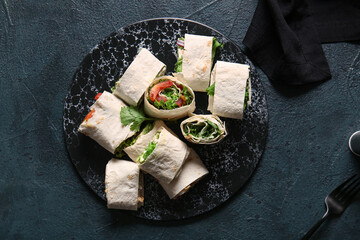 Board of tasty lavash rolls with vegetables and greens on black background