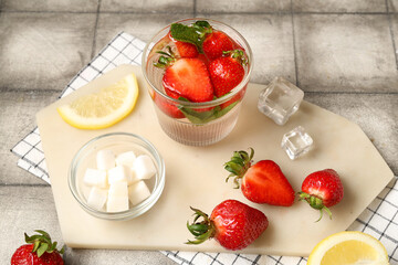 Board with ingredients for preparing strawberry lemonade and glass of drink on grey tile background