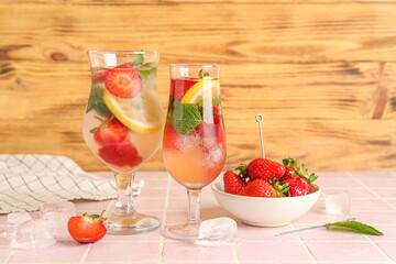 Glasses of fresh lemonade with strawberry and lemon on pink tile table