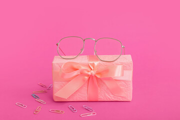 Gift box with eyeglasses and paper clips on pink background