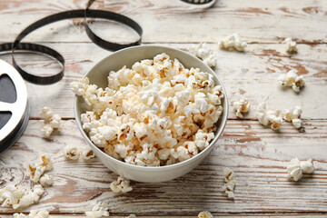 Bowl with tasty popcorn and film reel on white wooden background