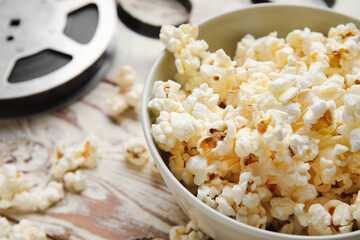 Bowl with tasty popcorn and film reel on white wooden background, closeup