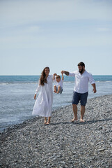 A happy European family enjoys a vacation at sea. The parents hold their son's hands and lift him up on the move. Mom and dad are playing with a child. The concept of a happy family, summer holidays.