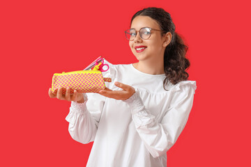 Female student with pencil case on red background