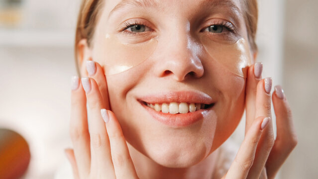 Hydrogel patches. Facial care. Anti-wrinkle cosmetics. Closeup of happy cheerful woman applying golden collagen under eye pads on clean face skin.