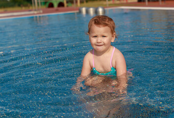 Little cute girl in a blue swimsuit in the pool. Active healthy lifestyle. Children on vacation on vacation. Baby 2 years old plays in the water outdoors.
