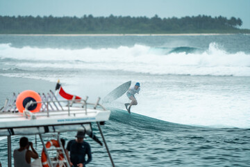 Naklejka premium Riding the Crest of Adventure: Surfer's Aerial Maneuver at Mentawai Islands, Indonesia, with Surf Boat Anchored in the Foreground