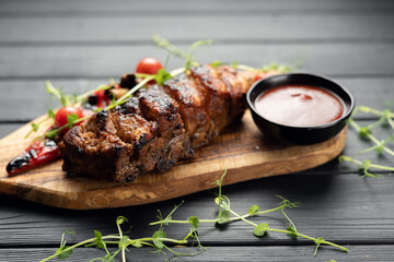Delicious barbecued ribs seasoned with grill vegetables and a spicy tomatoes sauce on wooden cutting board over dark background. Smoked American style pork ribs.