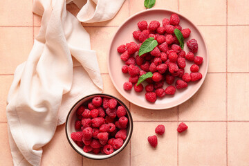 Plate and bowl with fresh raspberries on pink tile background