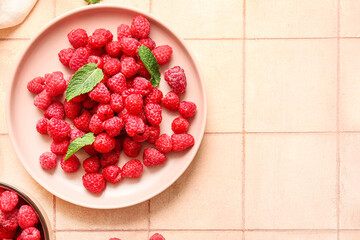 Plate with fresh raspberries and mint on pink tile background
