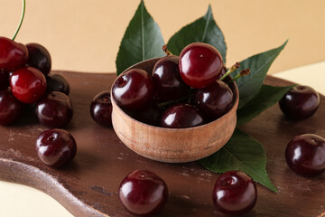 Wooden board and bowl with sweet cherries on beige background