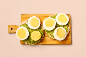 Wooden board of rice crackers with boiled eggs and avocado on pink background