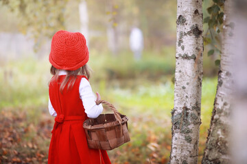 A little girl in a red hat and dresses is walking in the park. Cosplay for the fairytale hero...