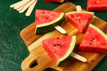Wooden board with sweet watermelon sticks on green background