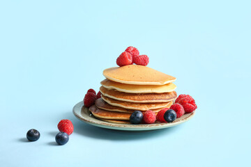 Plate of tasty pancakes with raspberries and blueberries on blue background