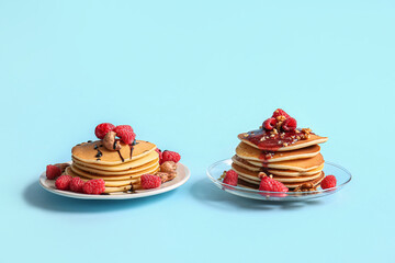 Plates of tasty pancakes with raspberries and nuts on blue background