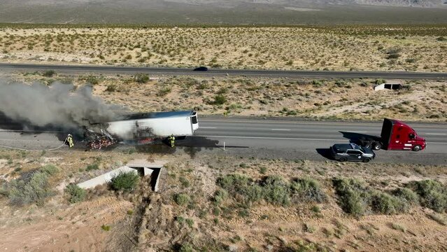 Aerial semi truck trailer fire highway firemen slide. Interstate highway in desert of Arizona and Nevada. Transporting fresh meat. Fire and smoke destroys cargo and HAZMAT pollution.