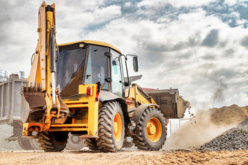 Powerful wheel loader or bulldozer against the sky. Loader transports crushed stone or gravel in a bucket. Powerful modern equipment for earthworks and bulk handling.