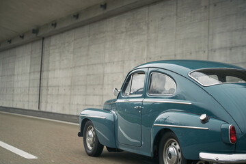 Plakat Old vintage European car model on the public highway. Blue oldtimer coupe speeding on the road.