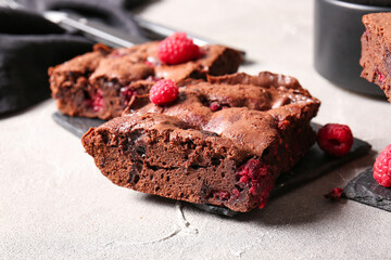 Board with pieces of raspberry chocolate brownie on grey table