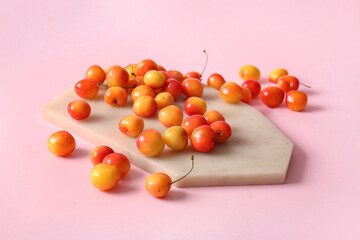 Board with sweet yellow cherries on pink background