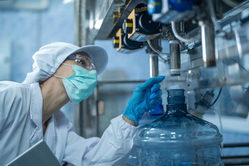 scientist worker checking the quality of water bottles on the machine conveyor line at the industrial factory. Female worker recording data at the beverages manufacturing line production.
