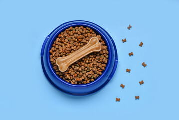 Bowl of dry dog food with chew bone on color background