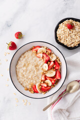 Bowl of oatmeal porridge with strawberry and banana on white table top view. Healthy and diet breakfast.