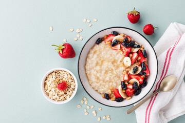 Bowl of oatmeal porridge with various berry and banana on blue table top view. Healthy and diet breakfast.