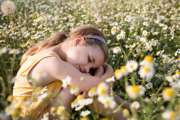a little girl in a yellow dress sits on a chamomile field on a summer day