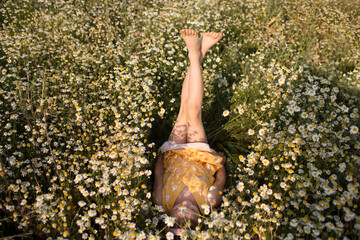 a little girl in a yellow dress  lies in the grass in a chamomile field