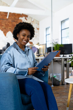 Portrait of happy african american casual businesswoman holding document folder in office