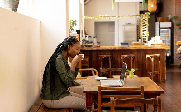 African american woman drinking coffee and using laptop in a cafe