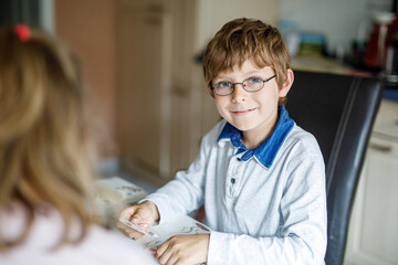 Active little school kid boy with glasses playing card game with his girl friend at home. Creative and funny leisure for elementary class children.