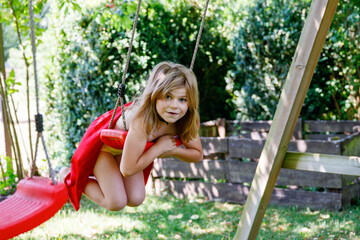 Happy little preschool girl in superwoman costume having fun on swing in domestic garden. Cute...
