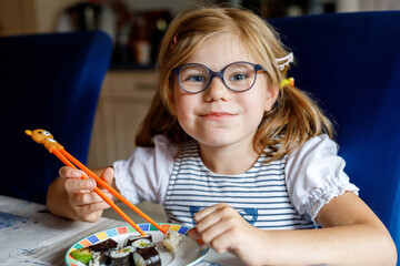 Happy Preschool Girl Eating Sushi Rolls at Home Using Chopsticks. Healthy Food for Children and...