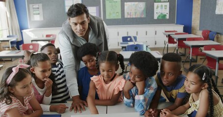 Happy diverse male teacher and children using laptop in elementary school class, slow motion - Powered by Adobe
