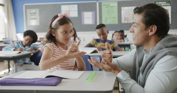 Happy diverse male teacher and girl practicing sign language in elementary school class, slow motion