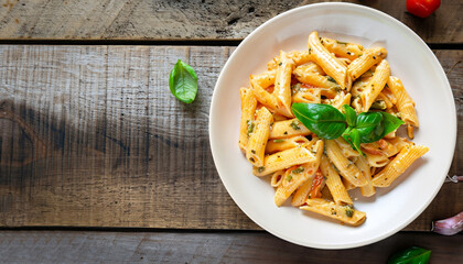 Delicious creamy Italian penne pasta starter with pepper seasoning and fresh basil viewed from above on rustic wooden centered with copy space