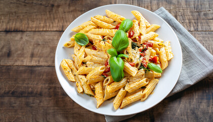 Delicious creamy Italian penne pasta starter with pepper seasoning and fresh basil viewed from above on rustic wooden centered with copy space