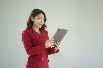 Beautiful Asian businesswoman in a red suit standing and holding a digital tablet over white background.