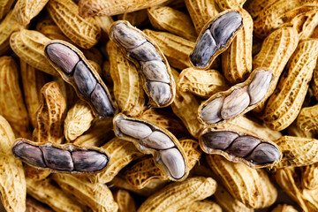 Unpeeled and peeled groundnuts on brown color background.